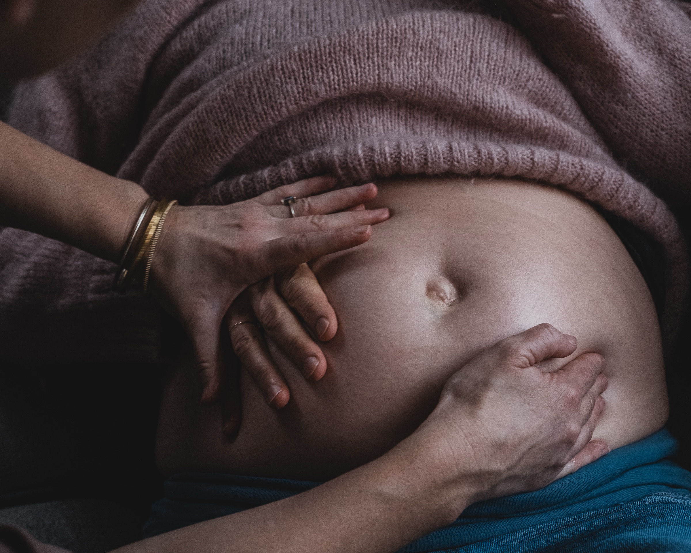 A midwife's hands resting gently on a mother's pregnant belly