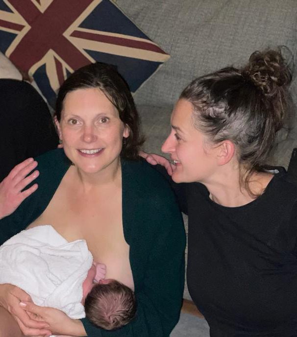 A mother breastfeeding her newborn, supported by her midwife