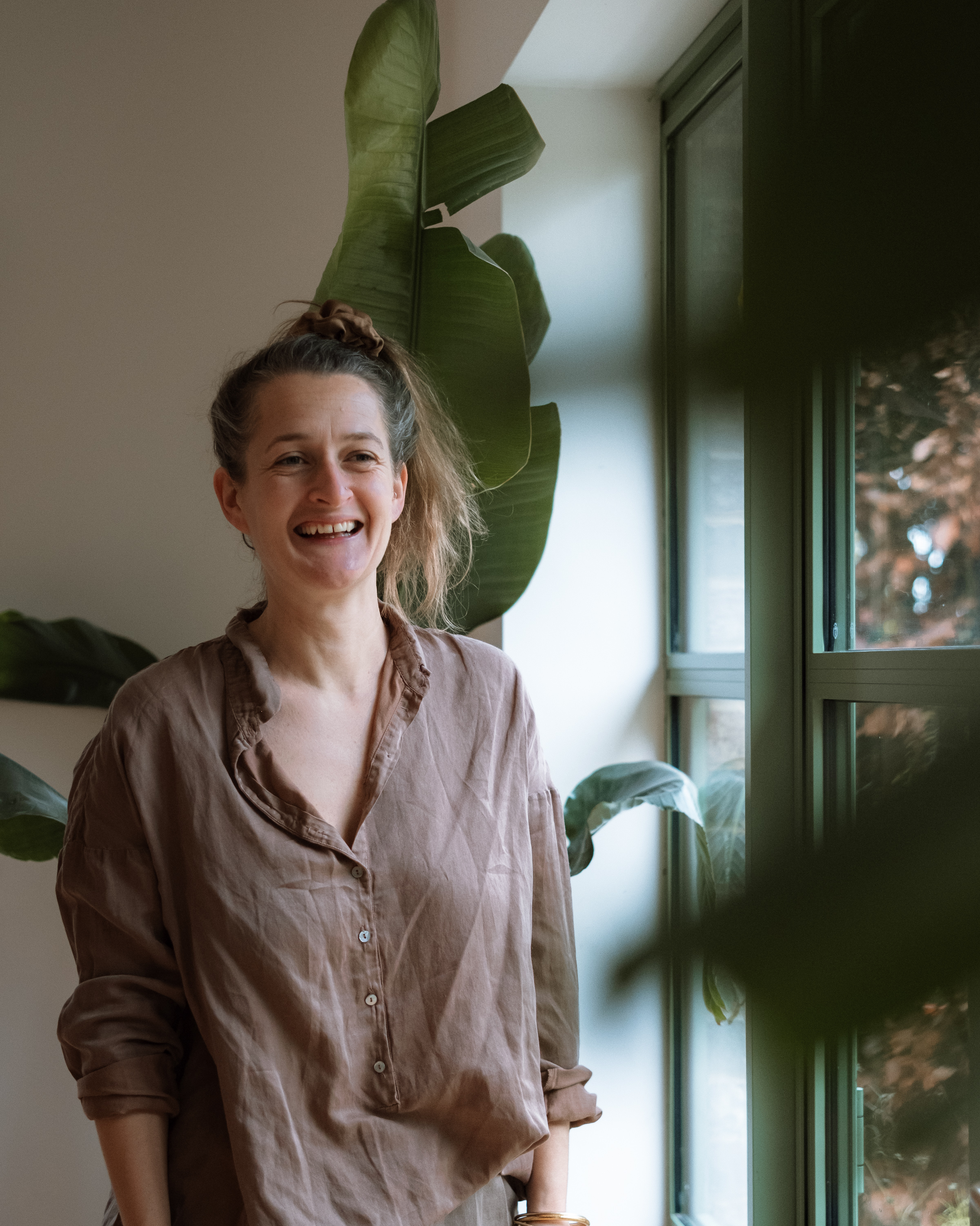 Rachel smiling warmly indoors, surrounded by houseplants