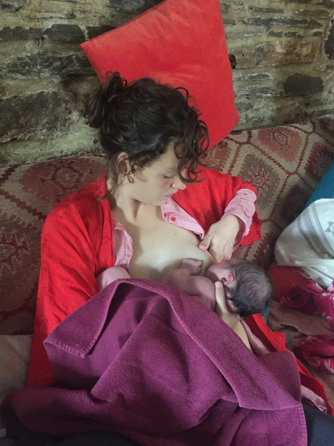 A mother breastfeeding her newborn, wrapped up together on the sofa